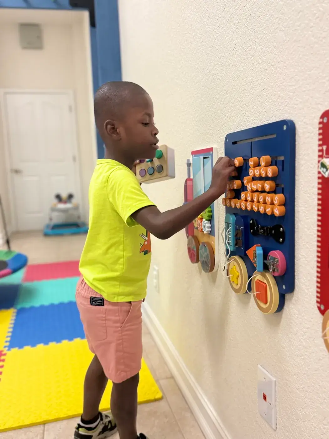 A boy exploring the wall-mounted busy boards in the hallway at Ellie's World PPEC in Port Charlotte, Florida