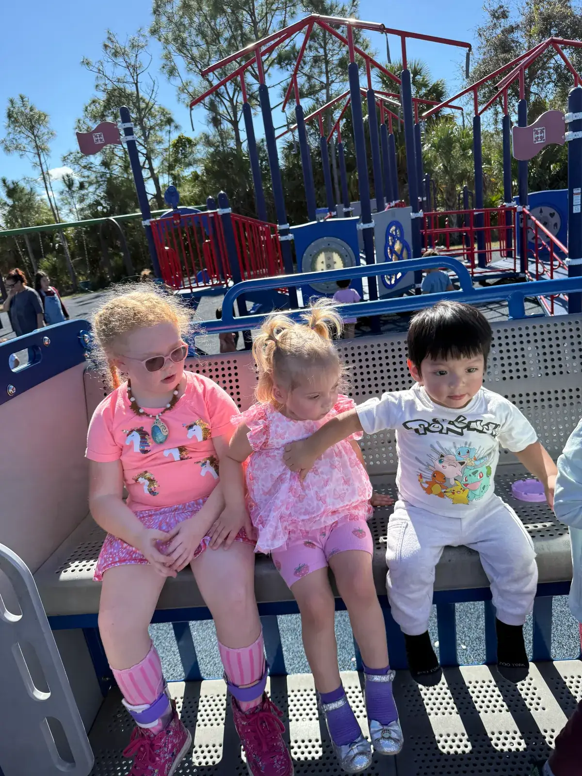 Three children sitting together on an accessible playground during a field trip near Port Charlotte, Florida