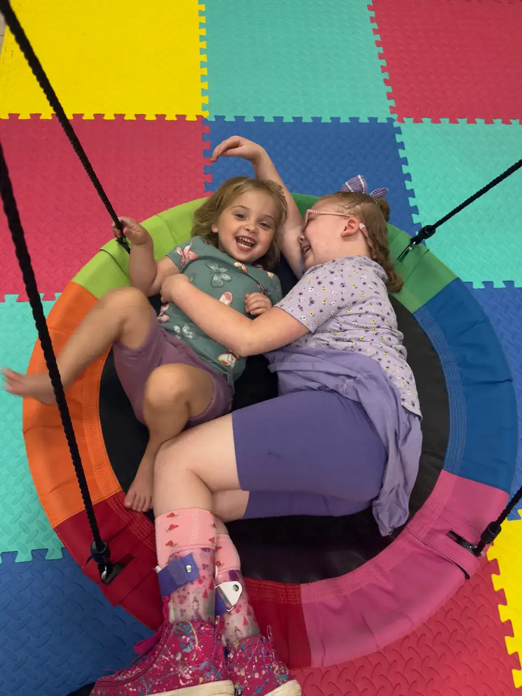 Two children laughing together on the indoor sensory swing at Ellie's World PPEC in Port Charlotte, Florida